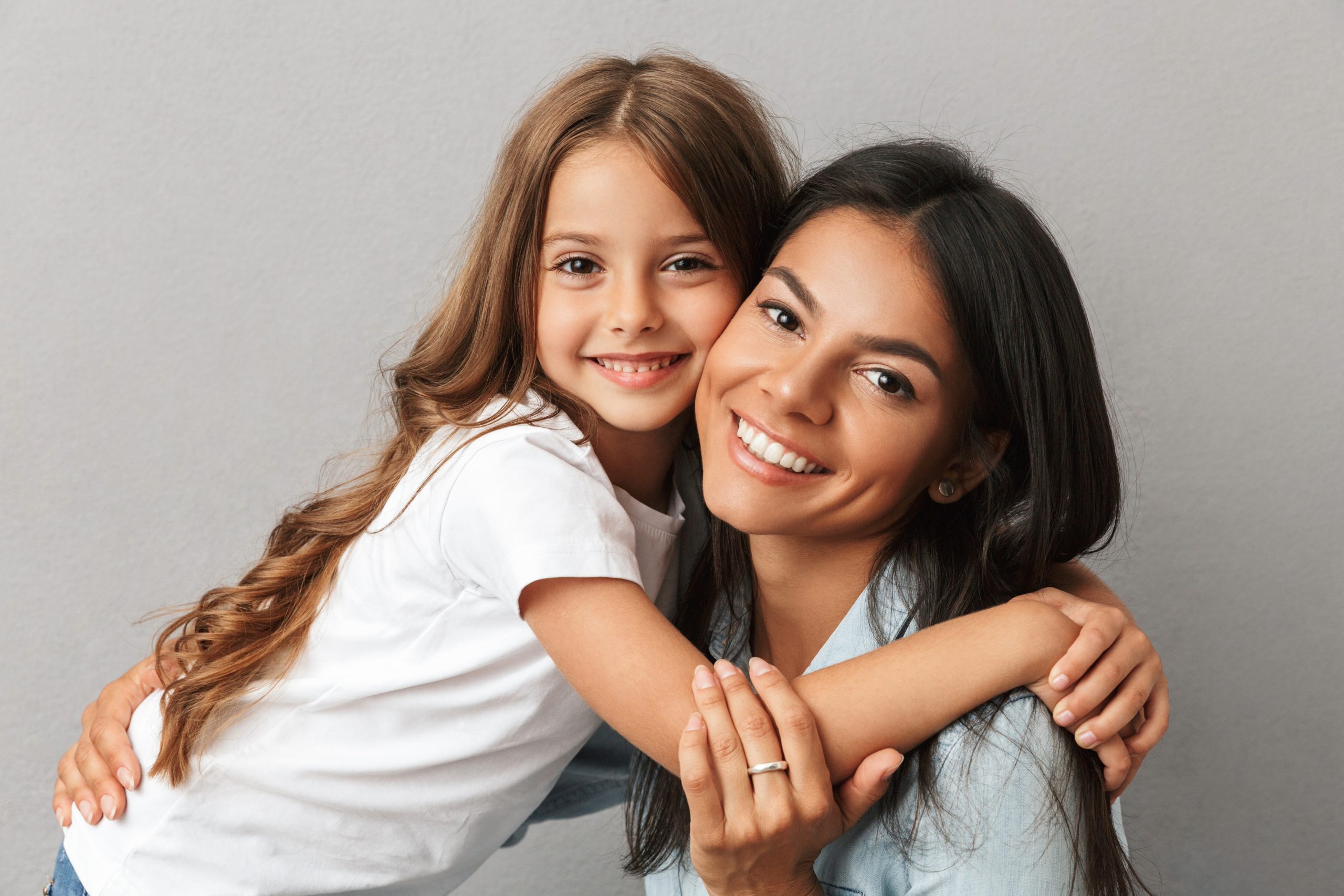 Photo of woman with little daughter smiling and hugging together, over gray background